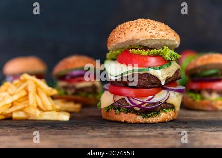 Hamburger doppio con pomodori, cipolle, cetrioli, lattuga, formaggio fuso e patatine fritte serviti su un rustico tavolo di legno Foto Stock