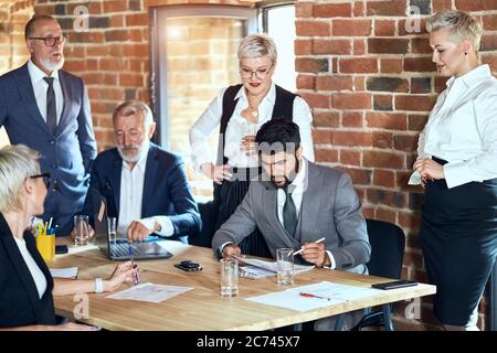 Gruppo di sei uomini d'affari caucasici indossano abiti eleganti in ufficio. La brunetta con la bearded al centro corregge le voci Foto Stock