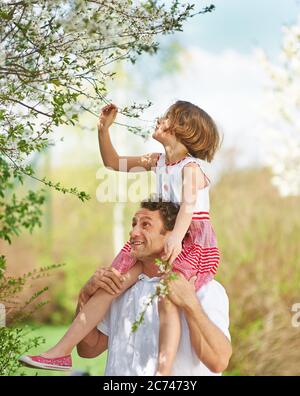 Padre porta sua figlia piggyback attraverso un parco in primavera Foto Stock