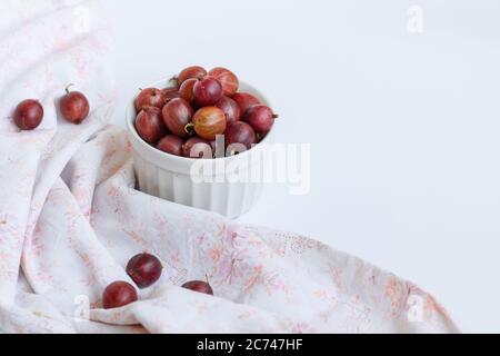 Le bacche di uva spina dolci maturate in un recipiente bianco su un tavolo bianco. Concetto di raccolto Foto Stock