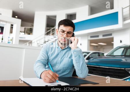 Il dipendente della concessionaria di auto sul posto di lavoro sta parlando al telefono. Foto Stock