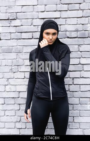 giovane sportiva musulmana in hijab in piedi vicino al muro di mattoni Foto Stock