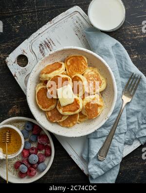 Pancake cereali, minuscoli e sottili briciole divertenti, cibo per bambini. Colazione con drink, tavolo scuro Foto Stock