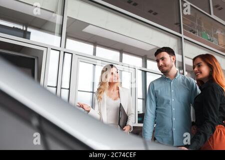 Il manager della concessionaria mostra le auto a una giovane coppia di famiglie Foto Stock