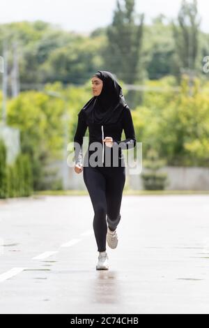 giovane atlantista musulmana in hijab e abbigliamento sportivo che fa jogging all'esterno Foto Stock