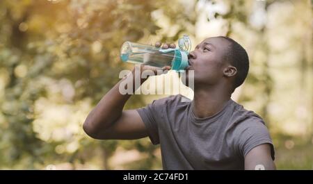 Giovane uomo nero che beve acqua da una bottiglia sportiva al parco Foto Stock