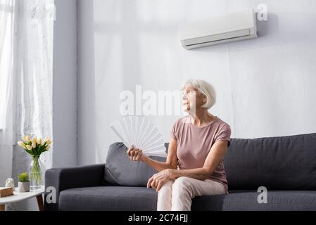 Donna anziana che tiene il ventilatore mentre soffre dal calore a casa Foto Stock