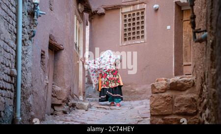 Abyaneh, Iran - 2019 maggio: Donna non identificata con abiti persiani tradizionali riposati su una strada stretta Foto Stock