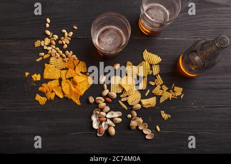 Su tavolo di legno scuro sono patatine, nachos, noci e pistacchi, nelle vicinanze sono due bicchieri di lager chiaro e bottiglia Foto Stock