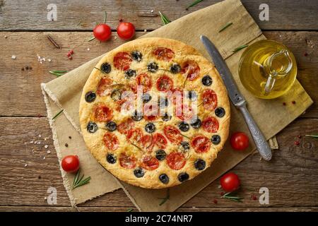 Focaccia, pizza, pane italiano piatto con pomodori, olive e rosmarino su tavola rustica in legno Foto Stock