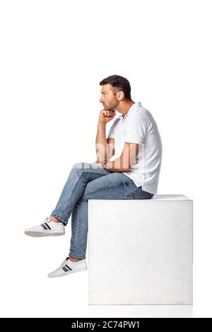 vista laterale dell'uomo pensivo in jeans denim seduti su cubo su bianco Foto Stock