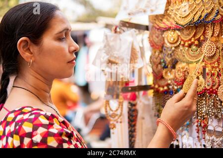 Donna matura indiana cercando e l'acquisto di orecchini, gioielli dal mercato di strada all'aperto di Delhi, India al giorno. È nel suo dres indiano tradizionale Foto Stock