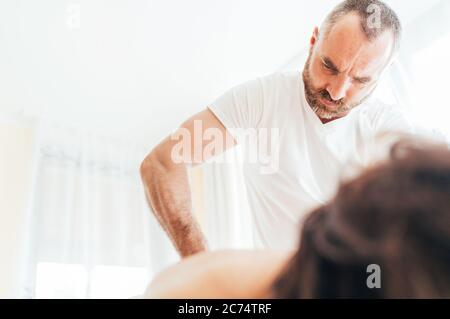 Uomo massaggiatore con braccio che effettua manipolazioni di massaggio sulla parte bassa della schiena durante il massaggio del corpo femminile. Immagine del concetto di assistenza sanitaria. Foto Stock