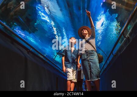 Madre e figlio camminano nell'enorme tunnel dell'acquario interno, godendo gli abitanti del mare sottomarino, mostrando interesse l'uno all'altro. Foto Stock