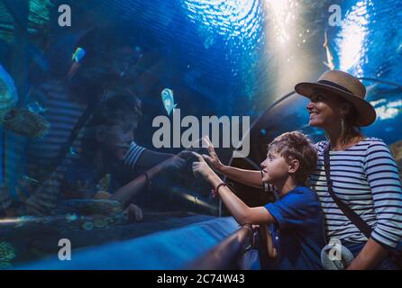 Madre e figlio camminano nell'enorme tunnel dell'acquario interno, godendo gli abitanti del mare sottomarino, mostrando interesse l'uno all'altro. Foto Stock