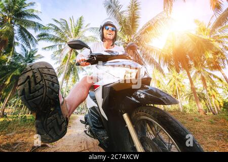 Uomo in casco sicuro che cavalcano moto in giungla. Immagine esotica concetto di vacanza. Foto Stock