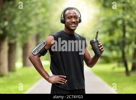 Giovane uomo nero che beve acqua mentre si allenano al parco Foto Stock