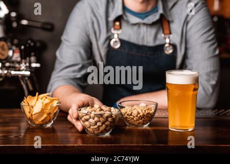 Spuntini croccanti dal barman. Pistacchi, noci e patatine in piatti e bicchiere di birra leggera con schiuma Foto Stock