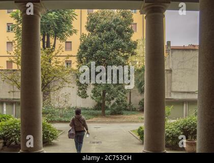 Vista di una turista femminile da dietro camminando attraverso il cortile di un palazzo di appartamenti a Milano, in Italia, la mattina presto. Foto Stock