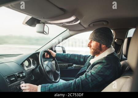 Uomo caldo vestito con bearded che guida auto moderna. Vista interna dell'auto. Guida invernale Foto Stock