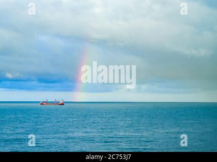 Arcobaleno in mare dopo pioggia e temporali. Viste colorate dell'arcobaleno sullo sfondo del cielo, delle nuvole e dell'orizzonte del mare con un carico s Foto Stock