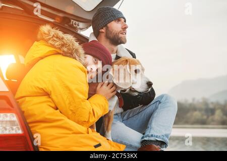 Padre e figlio con cane beagle che si siedono insieme nel bagagliaio dell'auto. Fine autunno Foto Stock