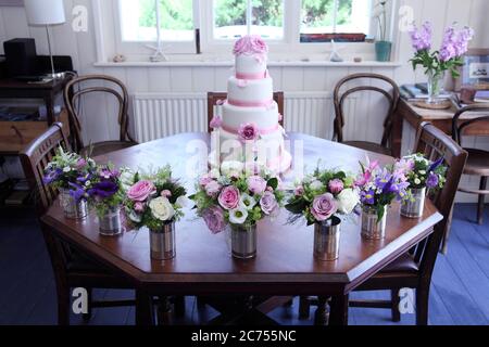 Torta di nozze ghiacciata rosa e bianca con rose di fiori di zucchero sulla parte superiore e bouquet di fiori in lattine di stagno di fronte. Foto Stock