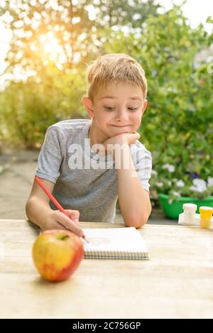 Il ragazzo carino disegna con matite ancora vita. Aria aperta. Giardino sullo sfondo. Concetto creativo. Foto Stock