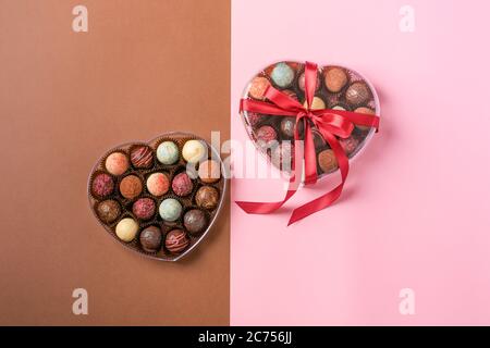 Caramelle al cioccolato tartufo fatto di cioccolato di diversi colori in una scatola a forma di cuore su sfondo rosa. Vacanza dessert Foto Stock