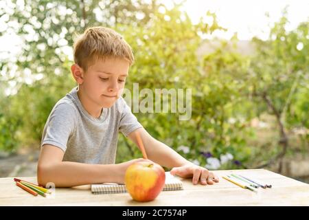 Il ragazzo carino disegna con matite ancora vita. Aria aperta. Giardino sullo sfondo. Concetto creativo. Foto Stock