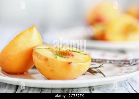 Pesche fresche fatte in casa arrostite cotte in zucchero di canna e sprigs di rosmarino fresco. Messa a fuoco selettiva con sfondo sfocato. Foto Stock