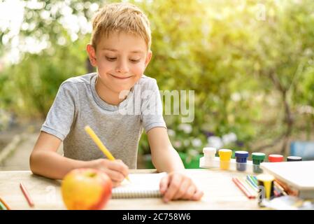 Il ragazzo carino disegna con matite ancora vita. Aria aperta. Giardino sullo sfondo. Concetto creativo. Foto Stock