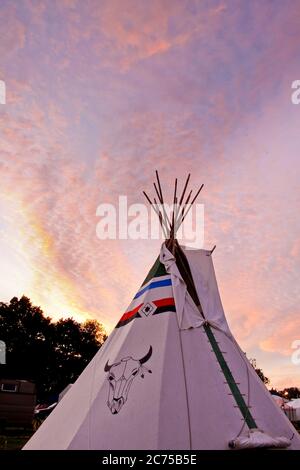 TIPI con decorazioni artistiche tradizionali di capi di bestiame dei nativi americani dipinte a mano in un campo glamping con in un campeggio festival al tramonto, Norfolk Foto Stock