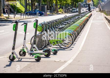 Una flotta di circa sessanta biciclette condivise Velib, insieme a tre scooter elettrici Lime, sono allineati ordinatamente in una stazione di attracco a Parigi, Francia. Foto Stock