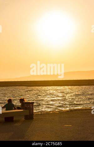 Persone che si godono un bellissimo tramonto sul mare, con un cielo giallo-arancione e onde calme sullo sfondo. marsiglia, a sud della francia Foto Stock