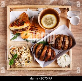 Delizioso pranzo all'aperto con stoviglie monouso su un vassoio di legno vista dall'alto. Foto Stock