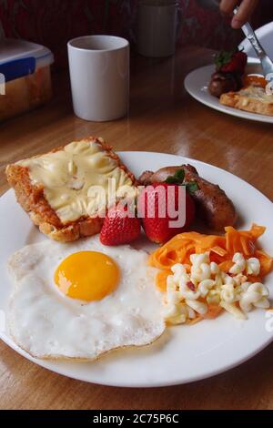 Delizioso toast al tonno al peperoncino con uova soleggiate, insalata di macaroni di carote grattugiate, salsiccia alla griglia e fragola. Foto Stock