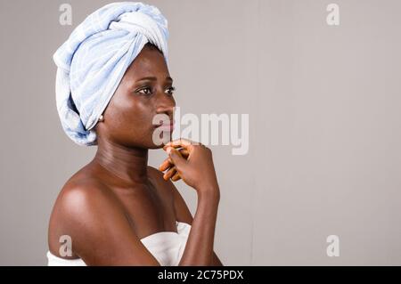 giovane donna in piedi su sfondo grigio tovagliato sulla testa che guarda penoso con la mano sotto il mento. Foto Stock