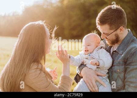 I genitori felici e il loro figlio trascorre del tempo in natura. Madre e padre tengono il bambino in braccio Foto Stock