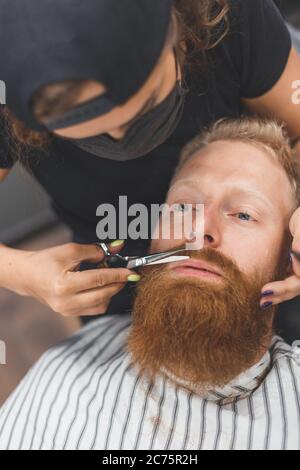 Un uomo in un barbiere. Baffi da taglio per barbiere donna. Barbiere donna in maschera. Foto Stock