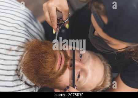 Un uomo in un barbiere. Baffi da taglio per barbiere donna. Barbiere donna in maschera. Foto Stock