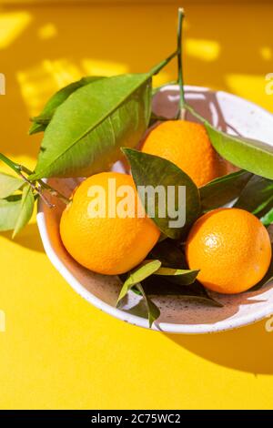 Arance intere con foglie di arance su sfondo giallo Foto Stock