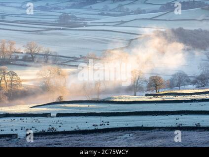 Mist over the River Wharfe is highlighted by the rising sun on a freezing winter morning overlooking Appletreewick in the Yorkshire Dales. Foto Stock