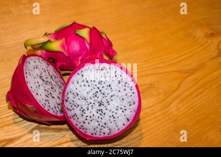 Un frutto di drago affettato e di colore bianco, conosciuto anche come Pitaya, su uno sfondo di legno lucido Foto Stock