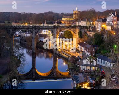 Le arcate del viadotto Nidd in Knaresborough glow orange contro la sera ore blu come un treno arriva in città dalla stazione ferroviaria. Foto Stock