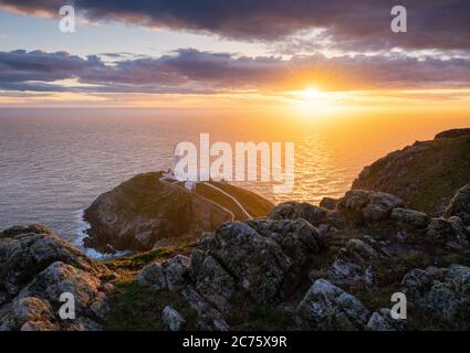 Il sole di setting highlights Sud pila faro sull isola di Holyhead, Galles, visto dalla rupe su una serata blustery in primavera. Foto Stock