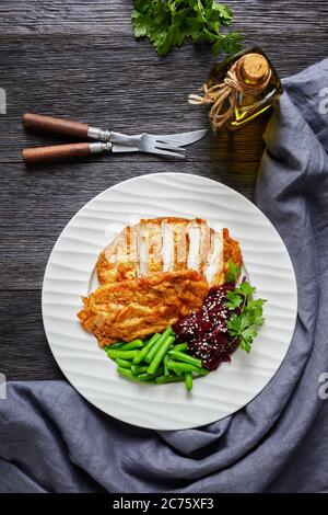 Schnitzel di pollo servito con insalata di barbabietole e fagioli verdi croccanti al vapore su un piatto bianco su un tavolo di legno scuro, vista verticale dall'alto, piatto la Foto Stock