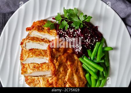 Schnitzel di pollo servito con insalata di barbabietole e fagiolo verde croccante al vapore su un piatto bianco su un tavolo di legno scuro, vista orizzontale dall'alto, piatto l Foto Stock