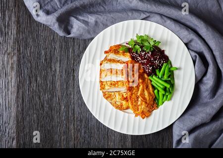 Schnitzel di pollo servito con insalata di barbabietole e fagiolo verde croccante al vapore su un piatto bianco su un tavolo di legno scuro, vista orizzontale dall'alto, piatto l Foto Stock
