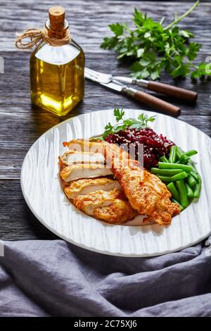 Schnitzel di pollo servito con insalata di barbabietole e fagiolo verde croccante al vapore su un piatto bianco su un tavolo di legno scuro, vista verticale dall'alto Foto Stock